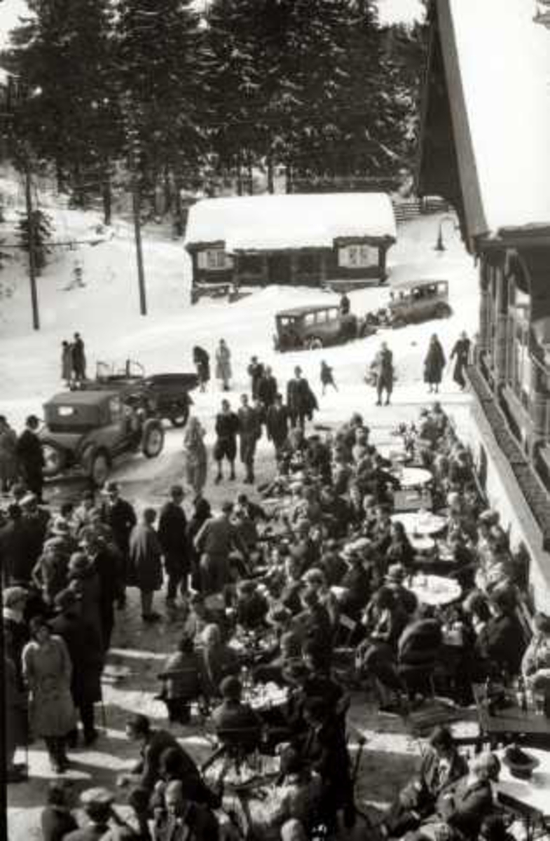Frognerseteren - Oslo. Vintermotiv. Mennesker ved bord foran restauranten. biler i bakgrunnen.
