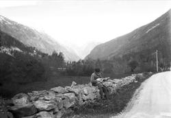 Fritjof Arentz sitter på et steingjerde og spiller på en man