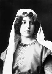 Studioportrett av kvinne i kostyme med slør og smykke rundt 