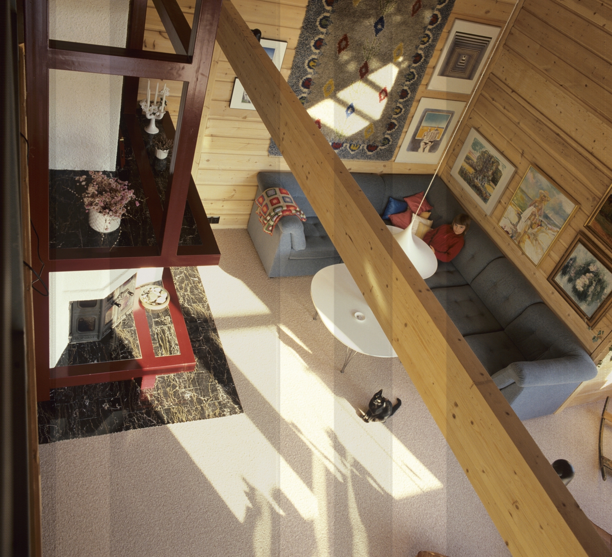 Stue med et sofahjørne, peis, veggteppe, lampe, bord og malerier på veggen, sett ovenfra i et hus. llustrasjonsbilde fra Bonytt 1986.