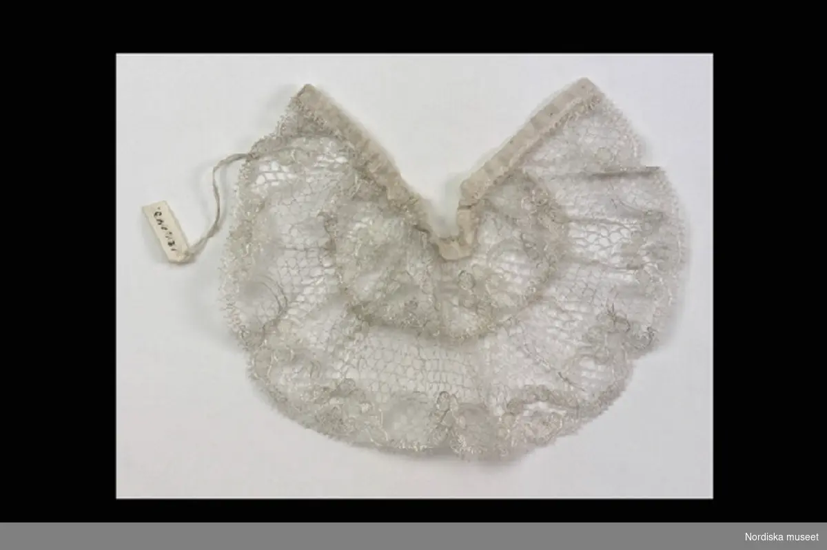Inventering Sesam 1996-1999:
L 7 cm
Dockkrage av vitt silke, knypplad, sk. blonde, ursp. spets av råsilke.
Helena Carlsson 1996