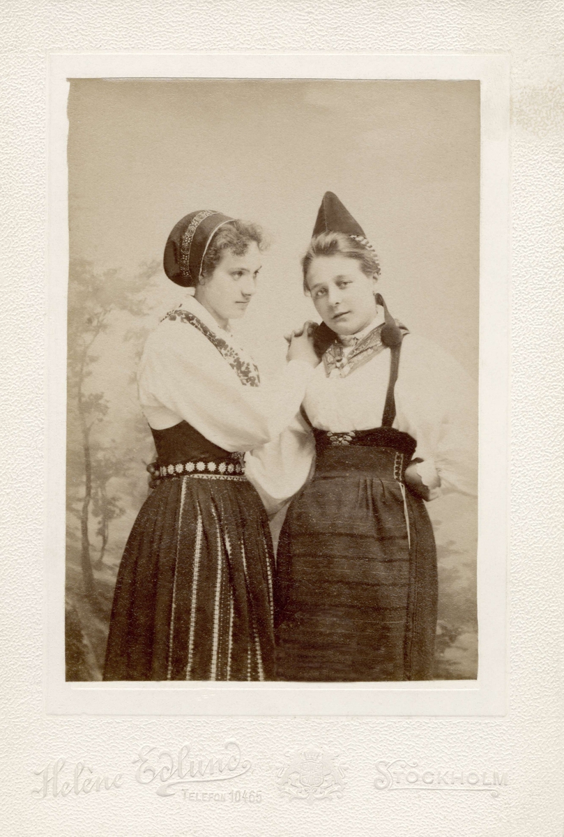 Två unga kvinnor poserar i olika folkdräkter