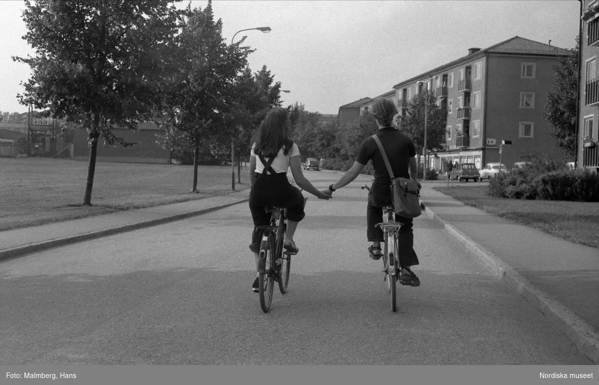 Ungt par cyklar på varsin cykel och håller varandra i hand.