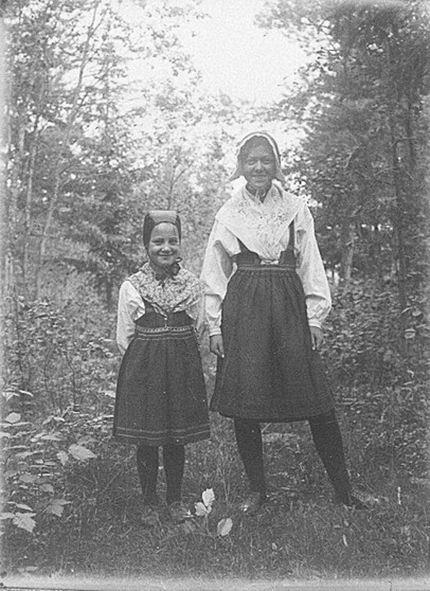 Porträtt av två flickor i folkdräkter i utomhusmiljö. Lima, Dalarna