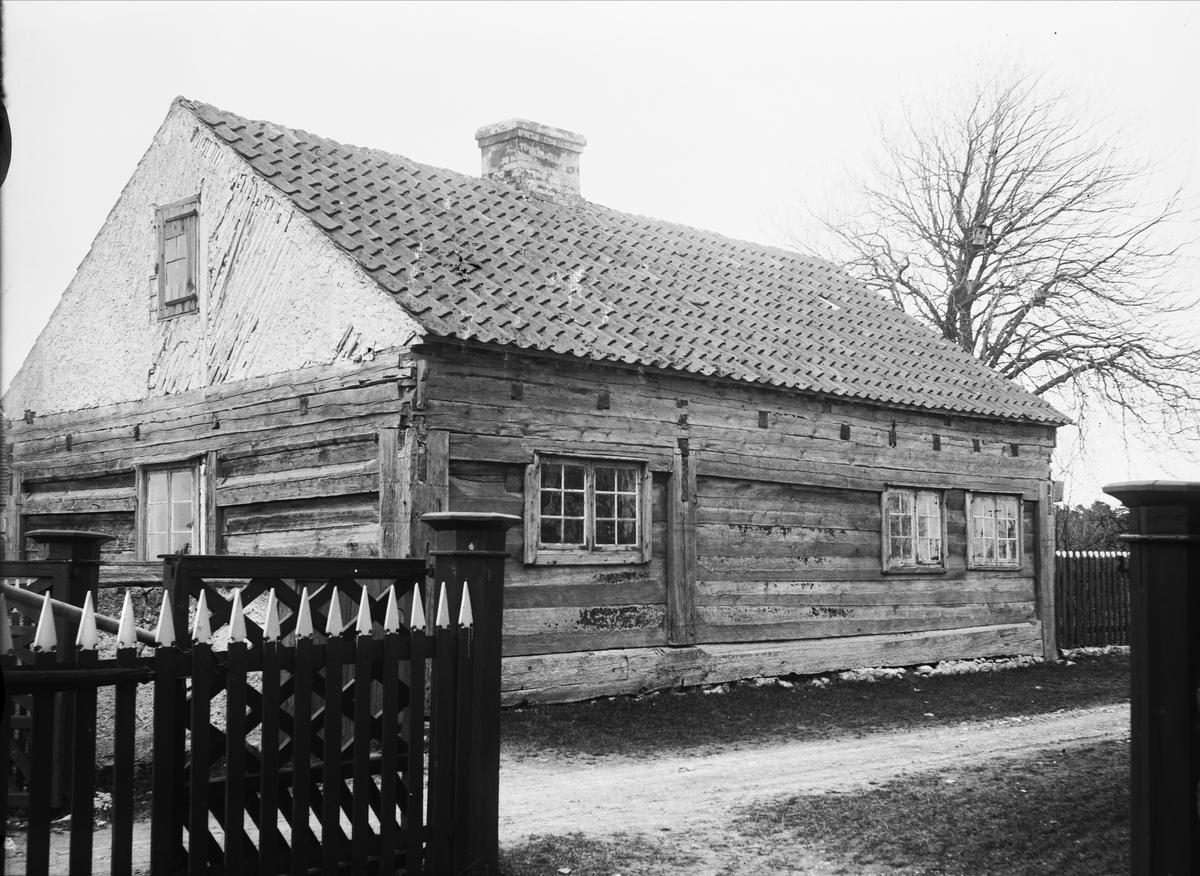 Lunderhaga gård i Fleringe socken, Gotland. Låg byggnad av liggtimmer med lerklinad gavel. Framför huset ett staket med öppnad grind.