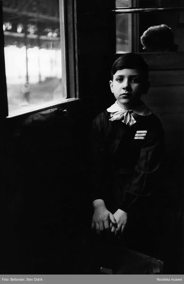 Välkammad pojke med skoluniform och skolväska sitter på ett tåg.