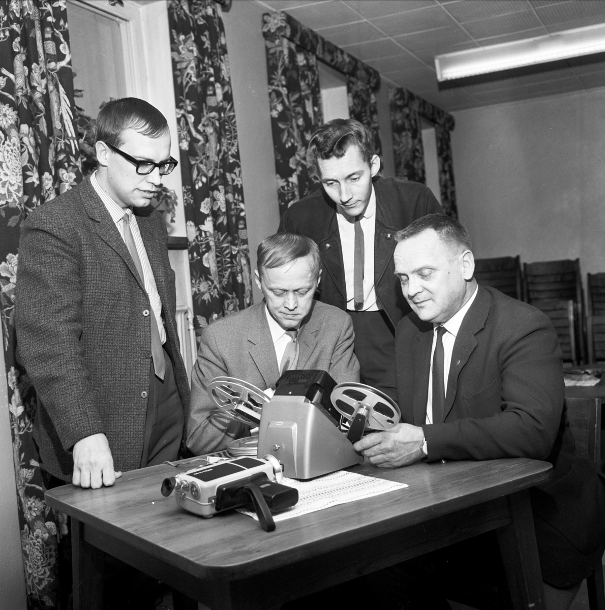 Göran Ekström, Ove Källblad och Söderfors fotoklubbs ordförande Torsten Lundin studerar den redigeringsapparat för smalfilm som Rolf Lundkvist demonstrerar