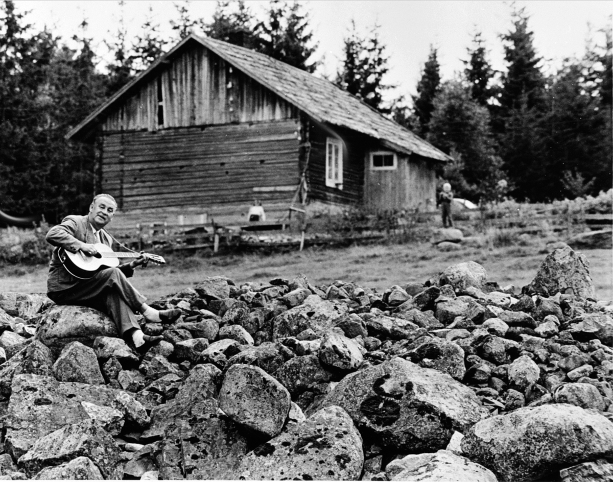 Alf Prøysen med gitar, steinrøysa neri bakken, Prøysenstua, Rudshøgda, Ringsaker.