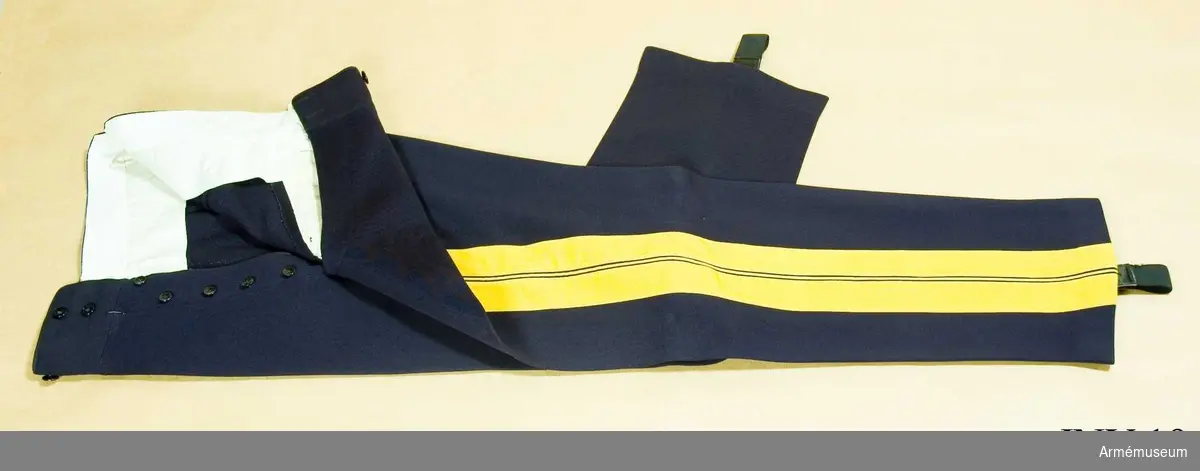 Av mörkblå diagonal. Revärer i gult kläde, 88 mm breda. Sidenfoder i linningen, två sidofickor. Gylfknäppning. 7 knappar. Hällor av resår.
Har tillhört Gustav VI Adolf (1882-1973).
