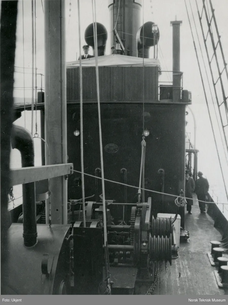 Ankerspill på dekk på hvalfangstskipet D/S Hektor II (senere omdøpt til Norman I), B/N 458 under prøvetur i Oslofjorden. Tre menn går rundt på dekk. Skipet ble levert av Akers Mek. Verksted i 1930 til A/S Hektor, ved skipsreder N. Bugge, Tønsberg.