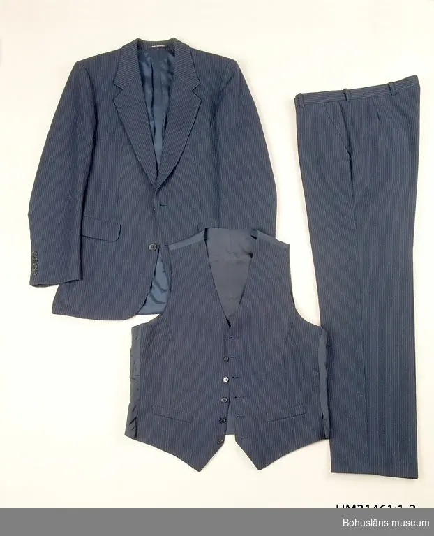 Mörkblå kostymkavaj (UM31461:1) sammanhörande med kostymbyxa (UM31461:2) och kostymväst (UM31461:3).
410 Mått ärmlängd 42 cm.

Mörklblå ull med smala kritstreck. 
Enkelknäppt med två knappar framtill, djup ringning. Infälld bröstficka på vänster sida, två fickor med ficklock fram.  I ryggen mittsöm, sprund i sidorna, baktill bildande vad som i folkmun brukar kallas "dasslock".  Knapphål på vänster slag. Fyra knappar på vardera ärm. Fyra invändiga fickor. Fodrad med mörkblå satin, ärmarna med vit randvävd satin. Passpoalstickningar runt kavajens kanter.
TygHängare i nacken med vävda texten: MADE IN SWEDEN
Firmaetikett i tyg på innerfickan texten: 
"TIGER
OF SWEDEN"
Firmaetikett i ena innerfickan, texten: 
"TIGER OF SWEDEN
STORL.
SIZE.
GRÖSSE  B 48.
451 26 UDDEVALLA