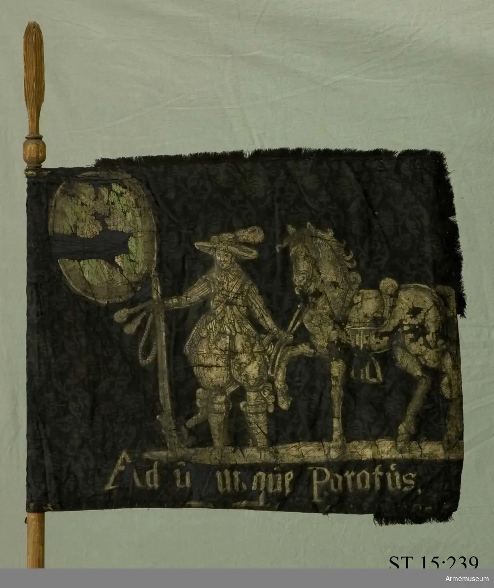 Fanduk av svart europeisk sidendamast med påmålad dekor i silver och grönt. Motivet är en dragon med hatt och kyller hållande en karbin i höger hand och i vänster en häst vid tygeln.
Text på framsidan: "Ad utumque paratus", på frånsidan "Hoffnung erhält mich".