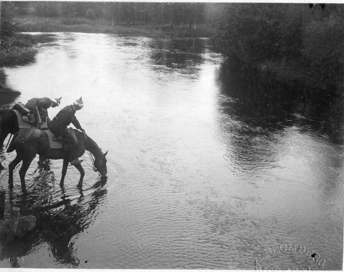 Två ryttare från Livregementet till Häst, K 1,  vattnar sina hästar vid Spångeån.