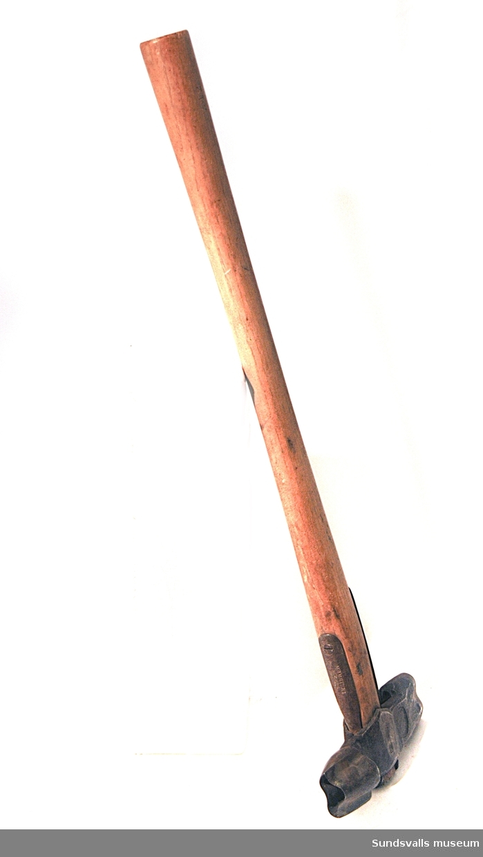 Märkyxa med träskaft. Huvudet mäter 19 cm och har oregelbundet formade huggmärken. Användes av Nyhamns AB.