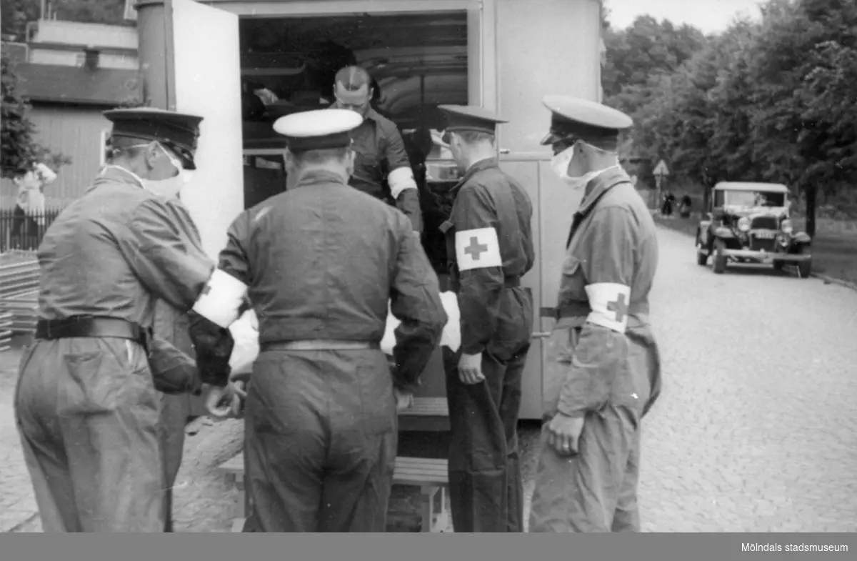 "Karantänsförläggning" på Kvarnbyskolan för överlevande från koncentrationsläger i Tyskland och Polen 1945.  
Skolan fungerade under denna sommar som beredsskapssjukhus.

Röda Korsets personal som hjälps åt att lyfta ut från buss eller ambulans, troligtvis en patient på bår.