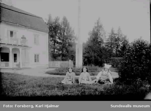 "Fru Bergkvist porträtterad med två flickor utanför herrgårdsbyggnad.