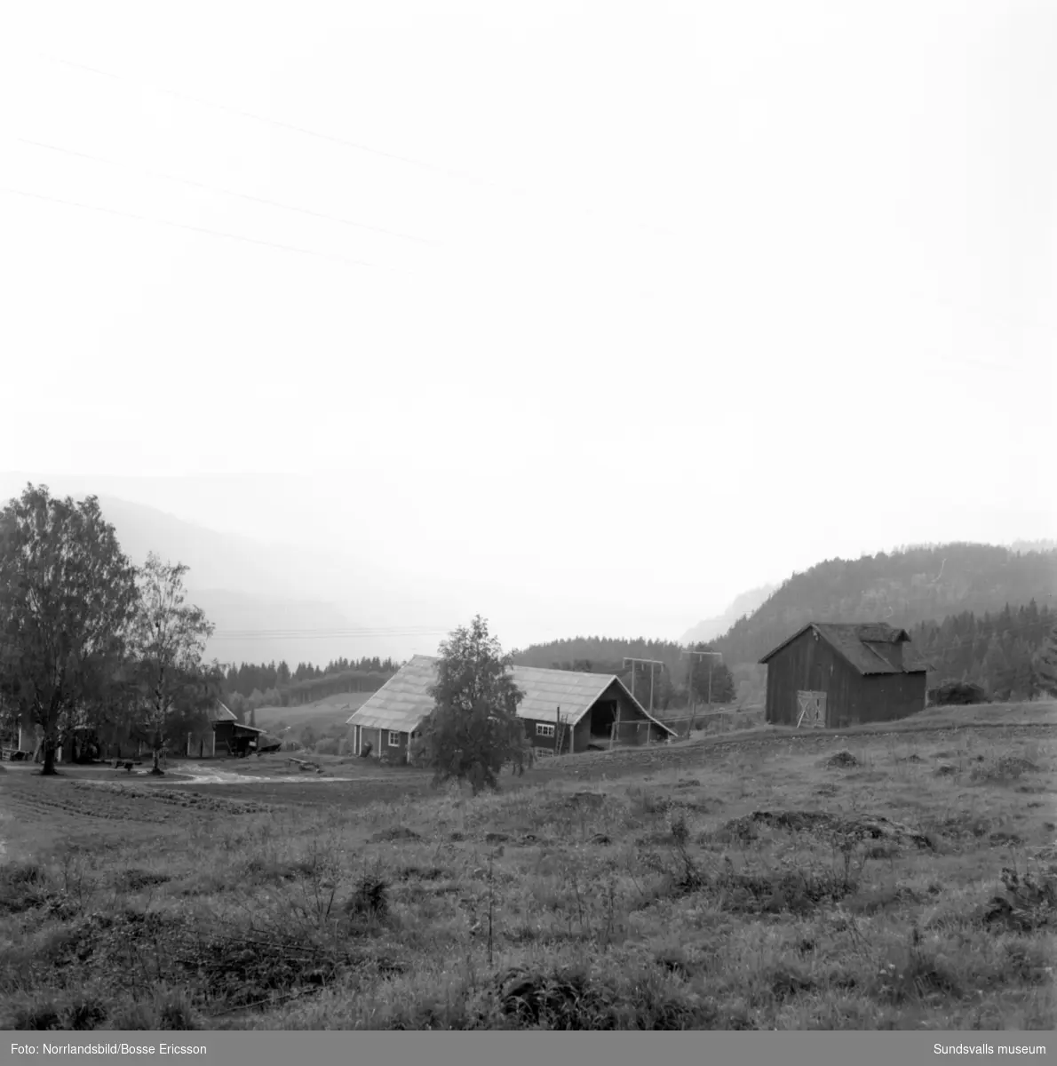Vy över Indalsälven och en gård på sluttningen i Järkvissle då regndimmorna ligger täta över älven.