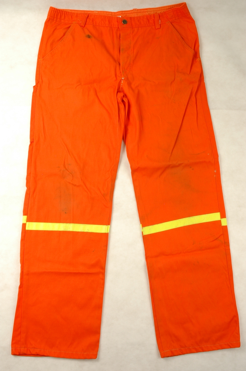 Jakke og bukse i oransje nylon/bomull sydd som arbeidsuniform. Jakken har påsydd emblem for Statens vegvesen foran på brystet. Det er påsydd refleksband på ermer og bukseben.