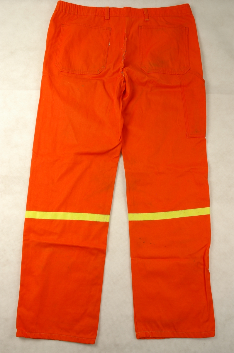 Jakke og bukse i oransje nylon/bomull sydd som arbeidsuniform. Jakken har påsydd emblem for Statens vegvesen foran på brystet. Det er påsydd refleksband på ermer og bukseben.