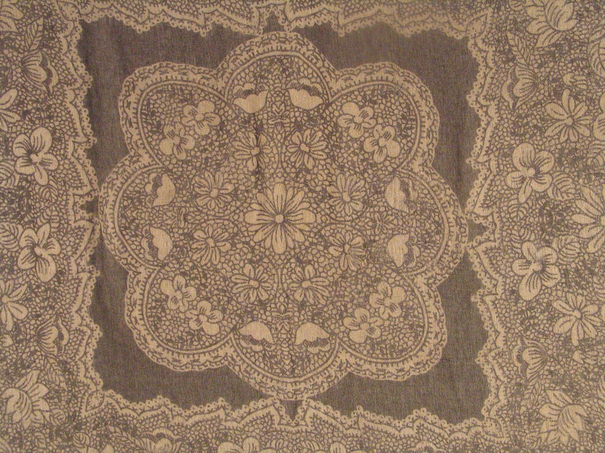 Stort blomstrefelt, utforma som ein blondeserviett, i midten. Breitt felt med same typen dekor rundt "servietten".