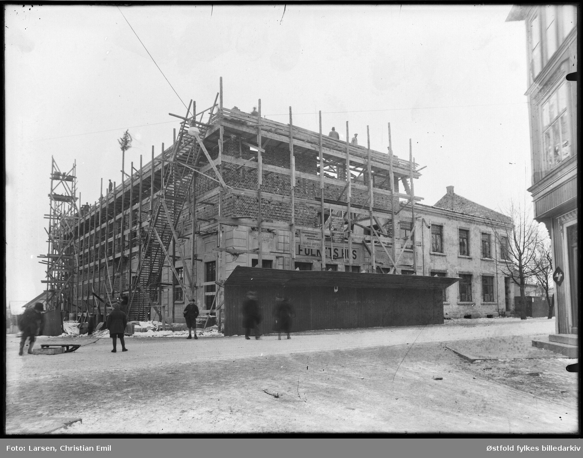 Tekst på eske. Utegrupper 1932-33. Folkets Hus i Sarpsborg under bygging.Kranselag (grantre på taket), arbeidere, stillas.