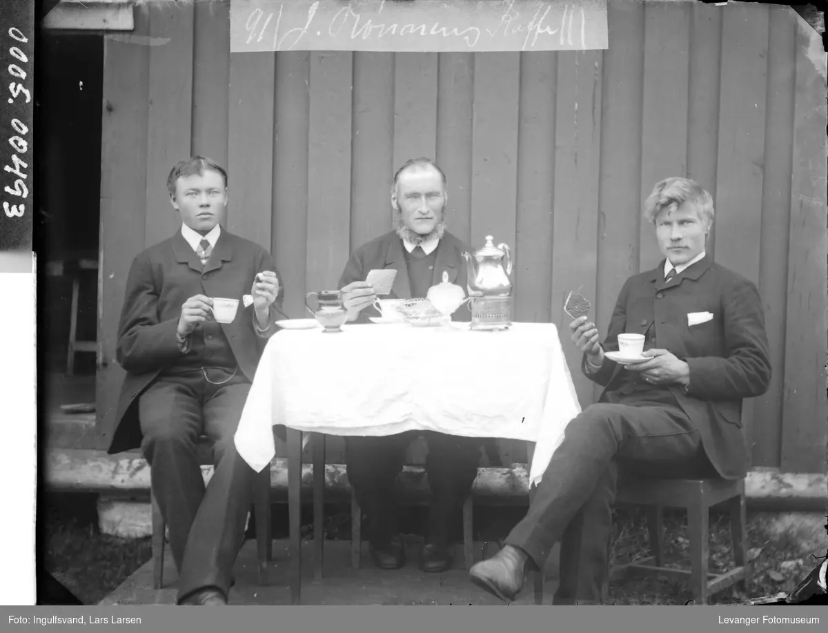 Gruppebilde av tre menn som sitter og drikker kaffe ved et bord.