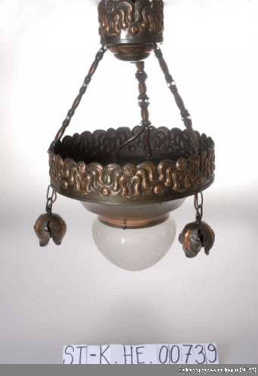 Taklampe hvor "stammen" er av messing og dekor i stilisert floral stil er preget inn i metallet. En glasskuppel sitter over lyspære i midten, mens tre lyspærer henger fra lampens ytterkant.