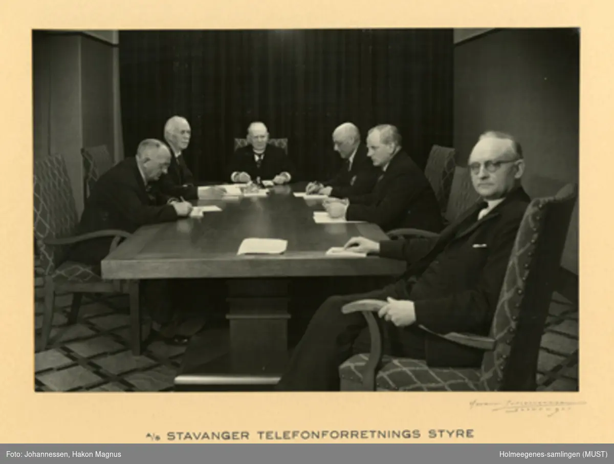 Gruppeportrett av seks menn rundt et møtebord. Stavanger telefonforretnings styre, mars 1941. Birger Pedersen lengst fra kamera. Foto montert på kartong i glass og ramme.
