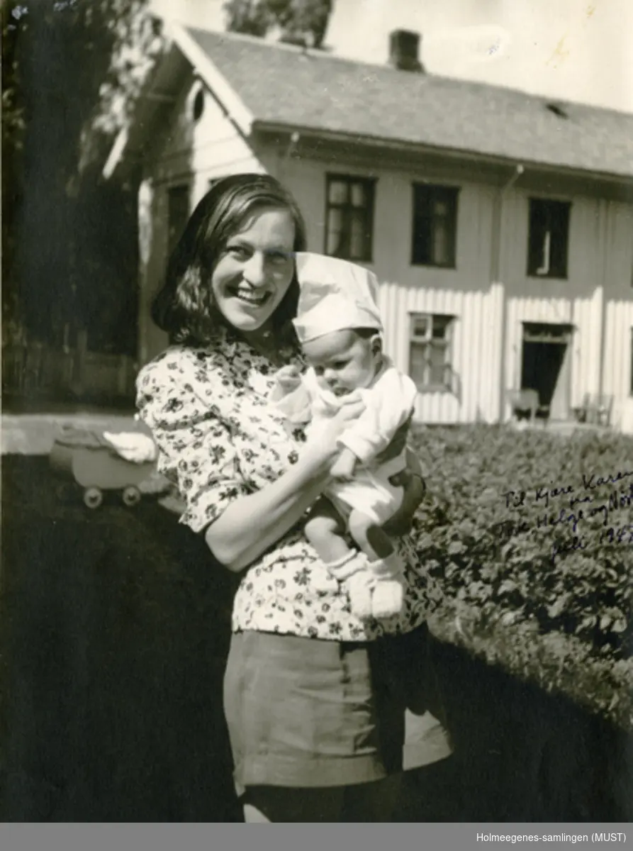 En ung kvinne med et spedbarn på armen, utendørs foran et bolighus. Påskrevet på bildet: "Til kjære Karen fra Tove, Helge og Nøste juli 1947".