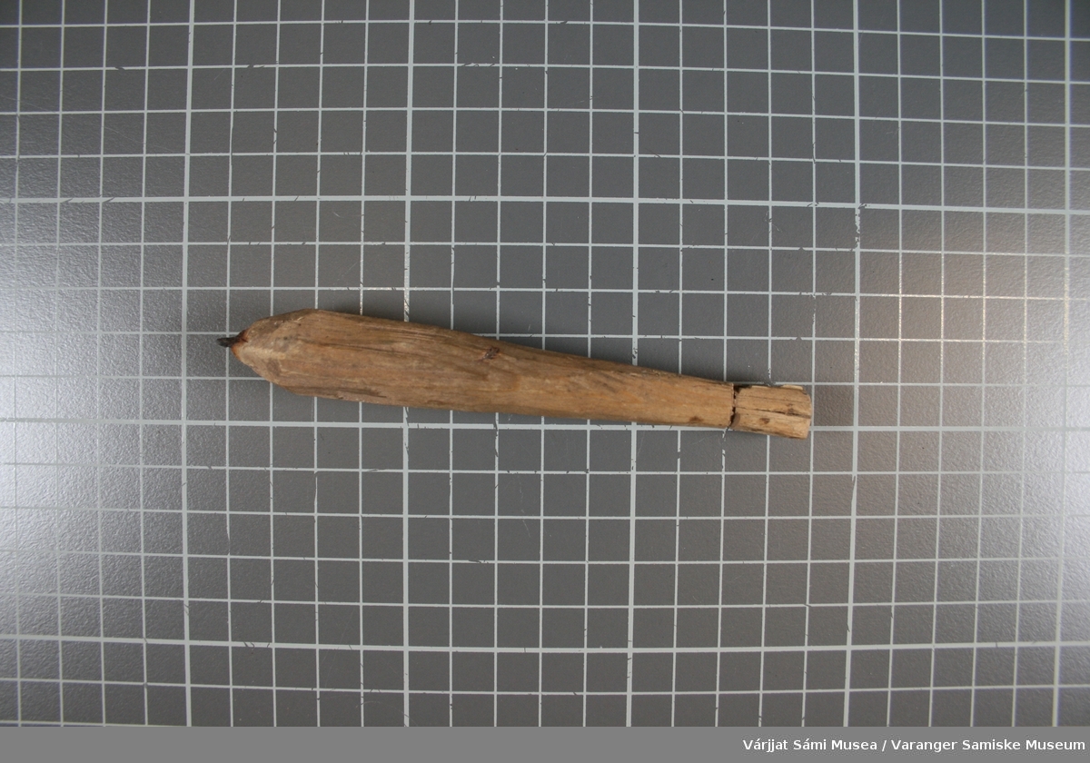 Pil laget av tre med en spiss av jern (rustent). Øverst er det et spor til å knyte et tynt tau ev. tråd i. Videre er det laget et kryss øverst til å legge et tynt papir eller lignende i.