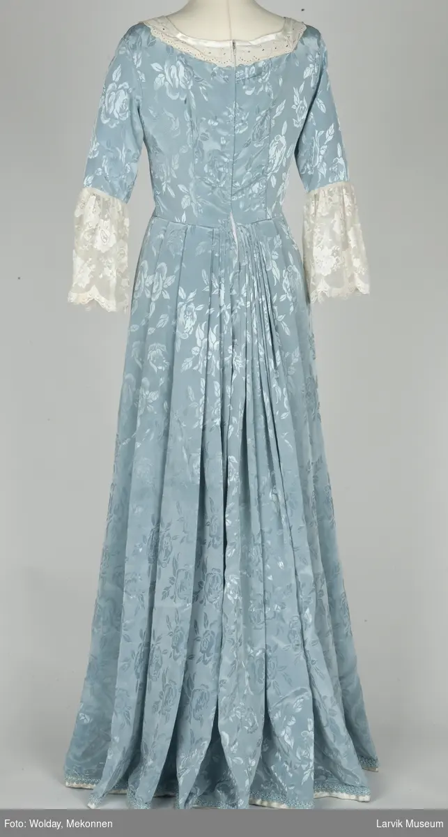 Lang kjole i lyseblå imitert silkeog blonder. Brukt som kjole/kappe under stivt underskjørt.