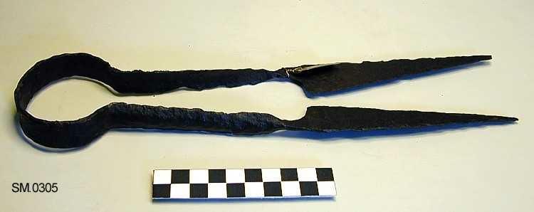 Fra protokollen: Saks av jern, sterkt rustet; jordfunden. 

Stor, med stor, rund og flat bøyle. (Rygh 443).Armene er flate, med svakt H-formet tverrsnitt, knivene lange, spisse, med rett rygg og eggsider som møtes i spissen. Overgangen mellom arm og kniv er svært skarp og brå. Tid: Antagelig Middelalder eller nyere tid. (Oldsakskatalog, J. S. Munch).