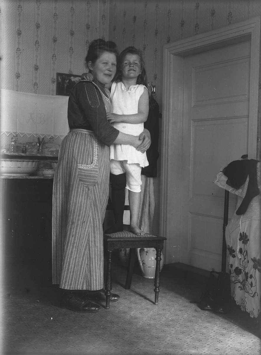 Interiør med stående kvinne og jente på en stol