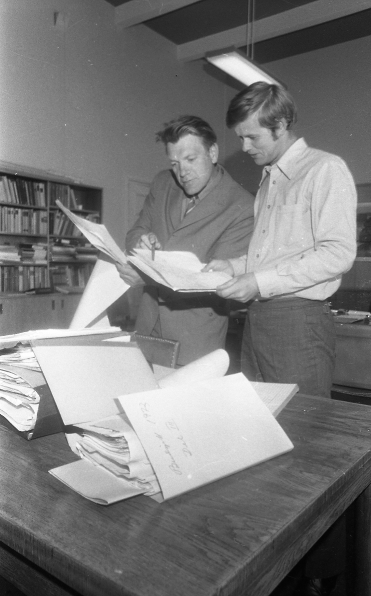To menn som studerer diverse sakspapirer.