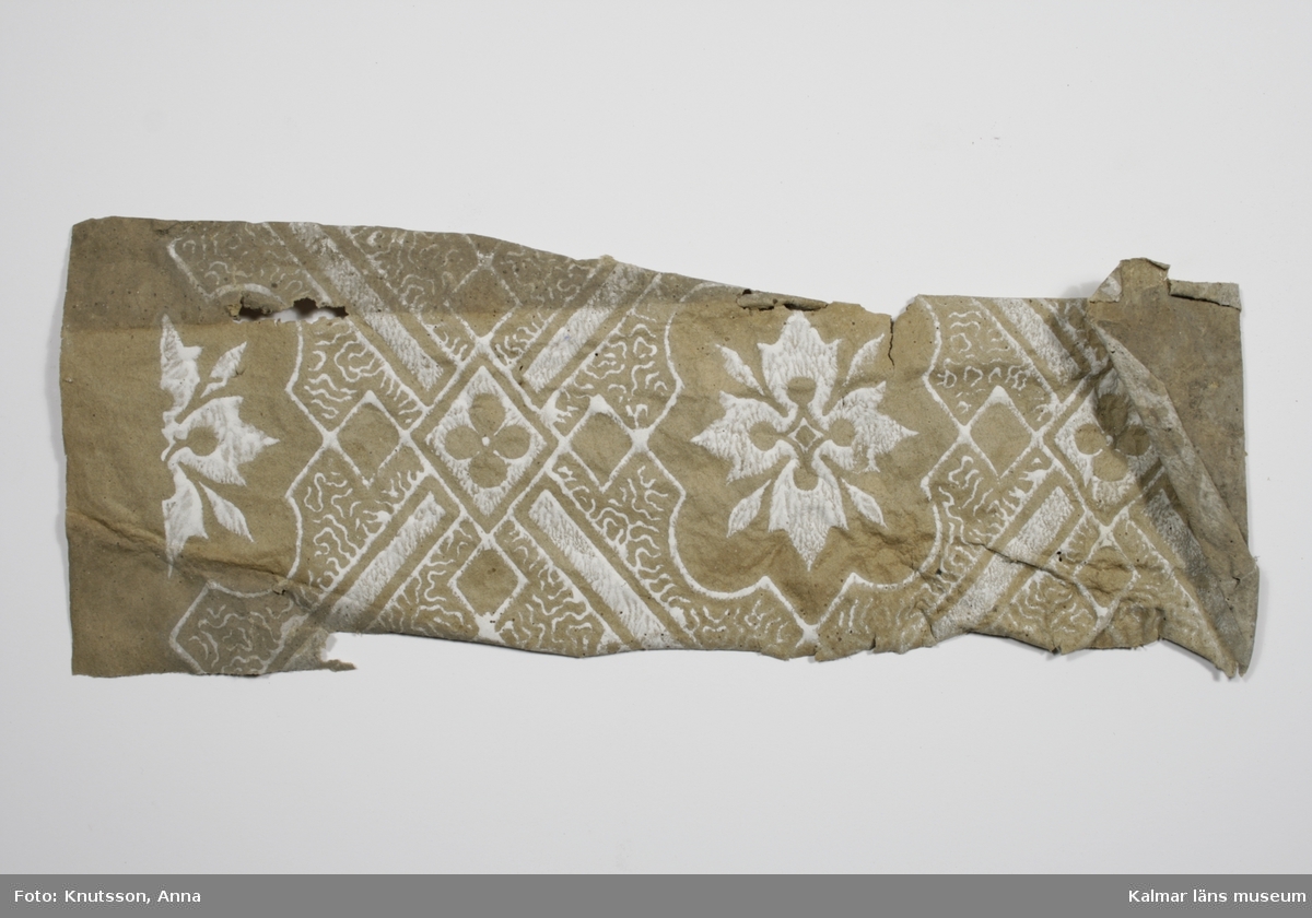 KLM 43790:2 Tapet i papper. 1 bit. Pappersfärgad botten med stiliserade blommor och mönster i vitt. Datering: 1860-tal.