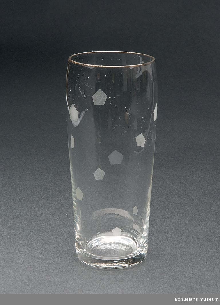 Högt dricksglas av klarglas med etsade Pripps-symboler strödda över ytan. Avsmalnande uppåt och med förgylld kant.