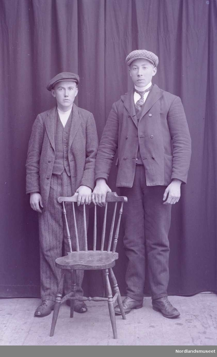 Portrett. To gutter står bak en pinnestol. Begge hviler sine ene hånd på stolens skulderbrett.