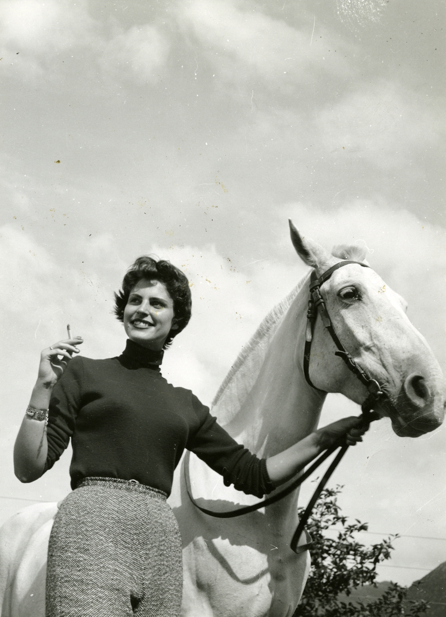 En kvinne holder en hest og røyker en sigarett.