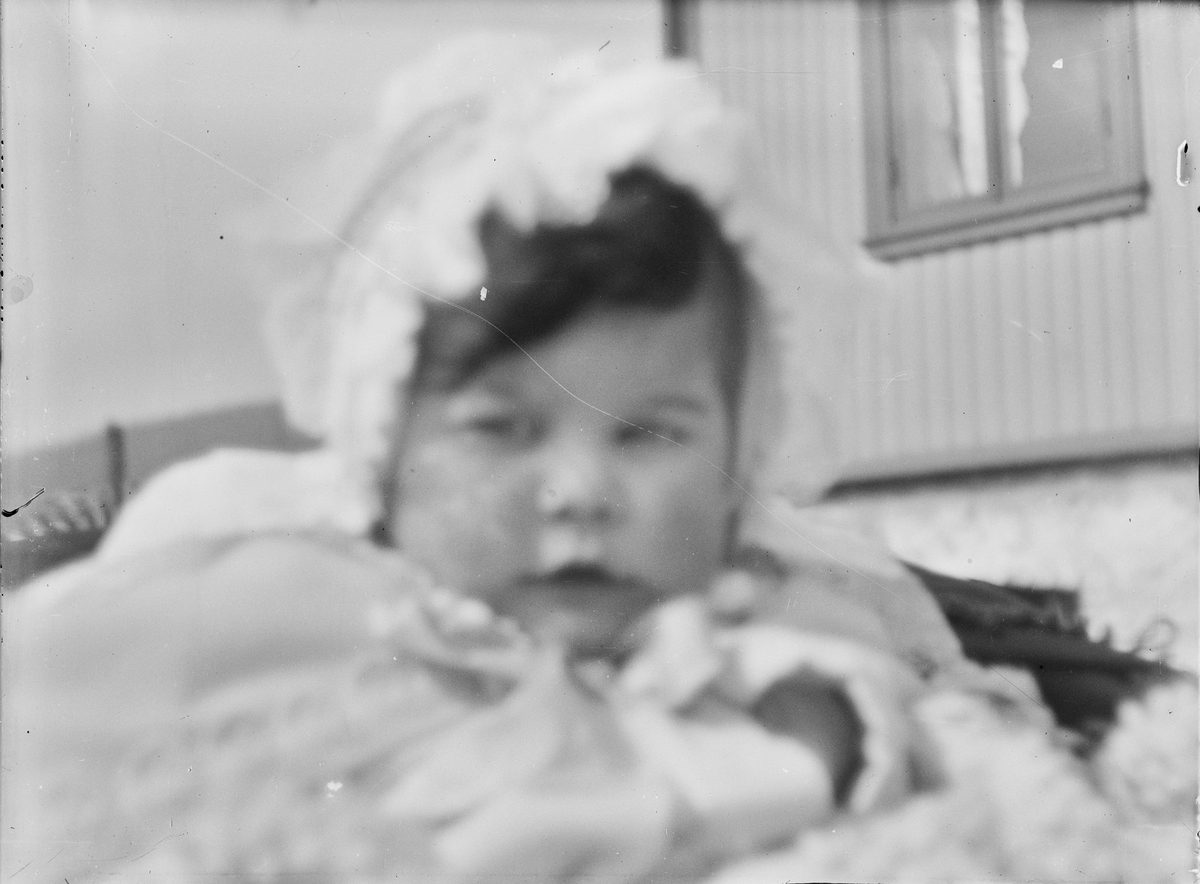 Nærbilde av et lite barn med blondekyse som sitter i en barnevogn utenfor et hus.