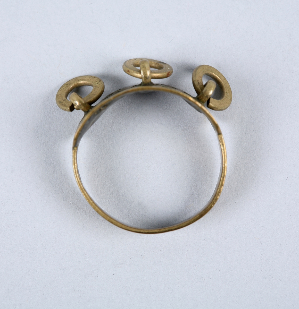 Fingerring av messing dekorert med 3 mindre ringar, lodda på fester på ringen. Overflata på ringen er dekorert med stempla punkt og strekar.
