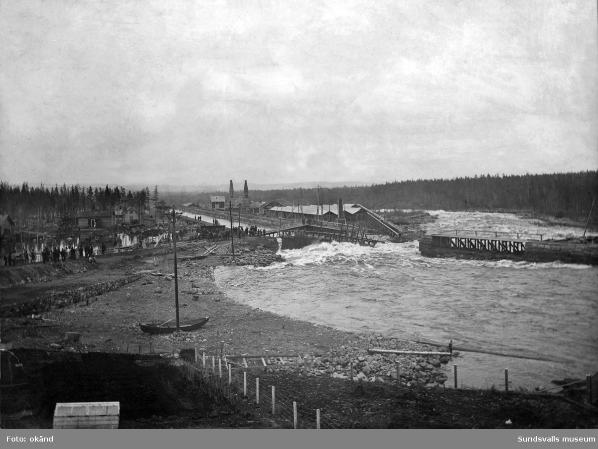 Alby kraftverksdamm våren 1906. En bristning i fördämningen har uppstått. I bakgrunden ses Alby karbidfabrik från 1901.
