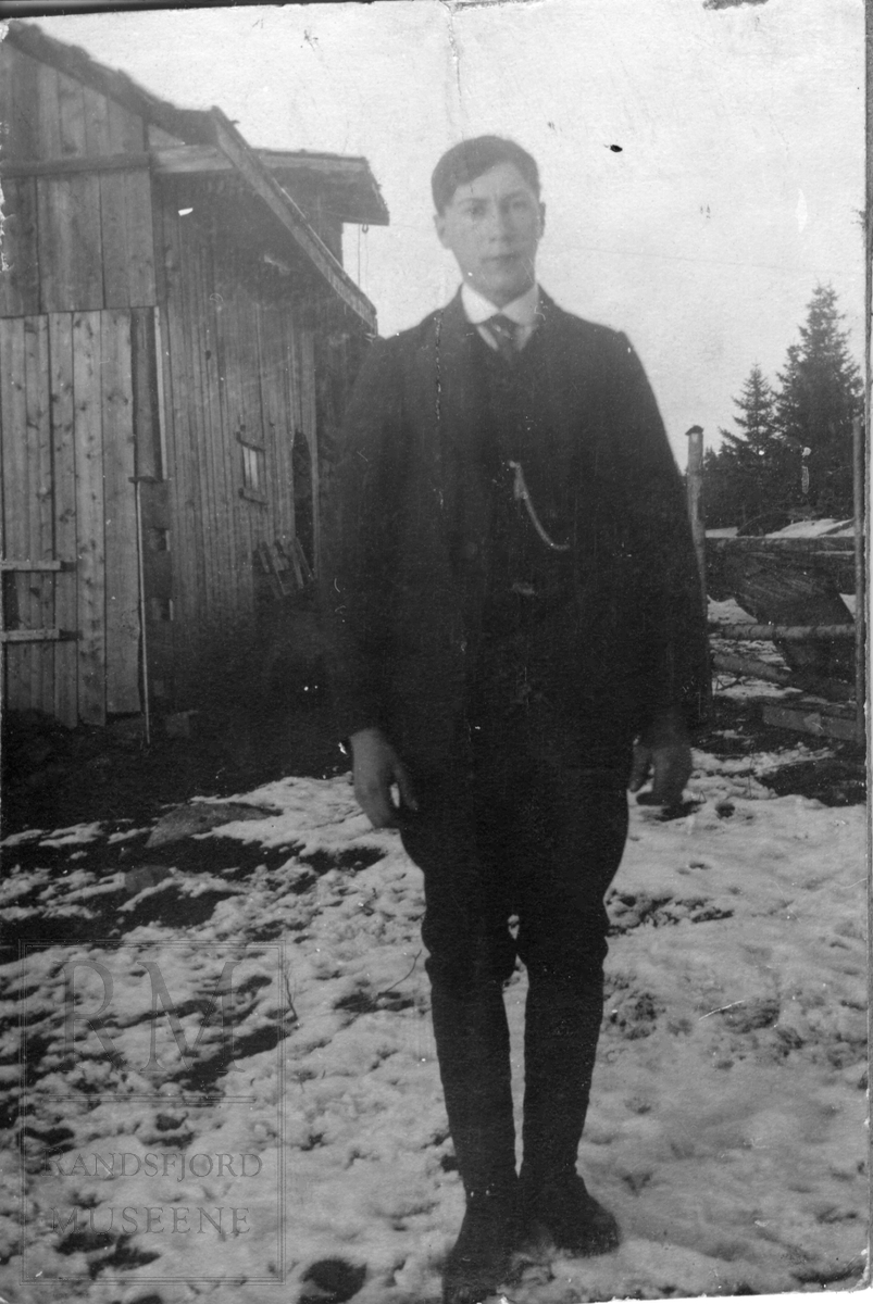 En ung mann stående foran en låve.
