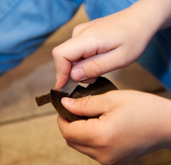 Nærbilde av barnehender som skjærer i en skinnbit med en steinflekke (Foto/Photo)