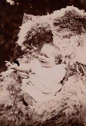 En baby (trolig Erica Mathiesen) sitter på et saueskinn i en