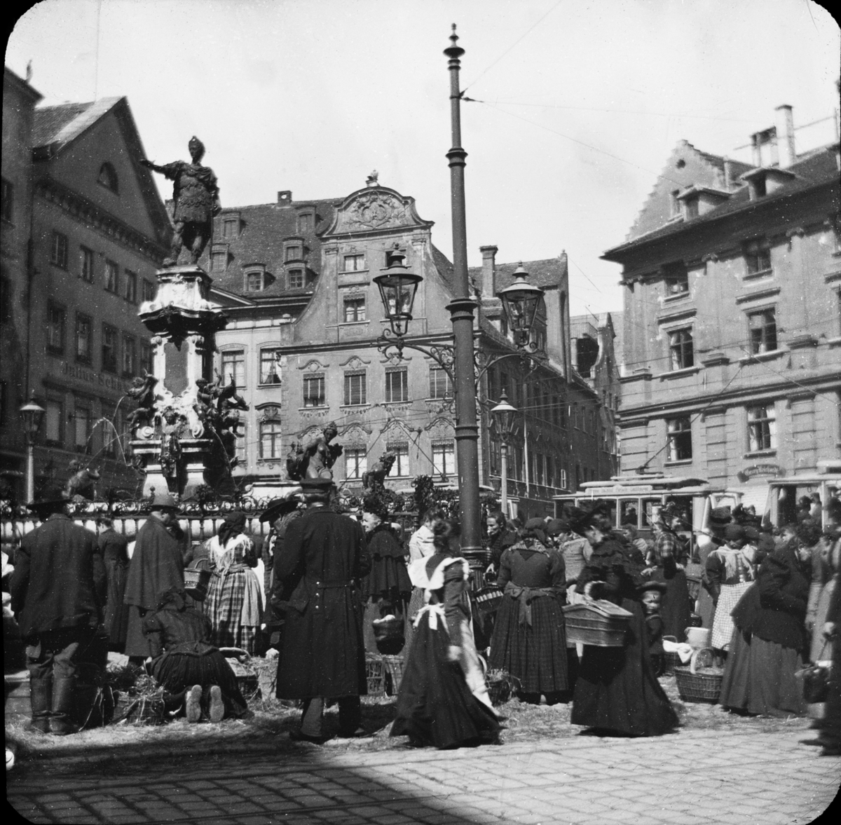 Skioptikonbild med motiv av Augustbrunnen, fontän på torget i Augsburg.
Bilden har förvarats i kartong märkt: Augsburg 1901. 13
