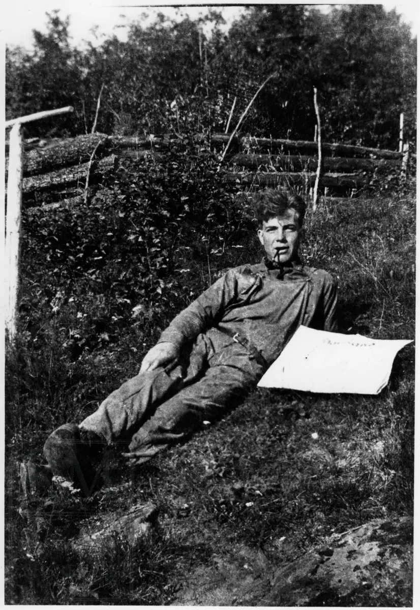 En mann med pipe, liggende i gresset med en avis. Personen kan være Bernhard Gransborg