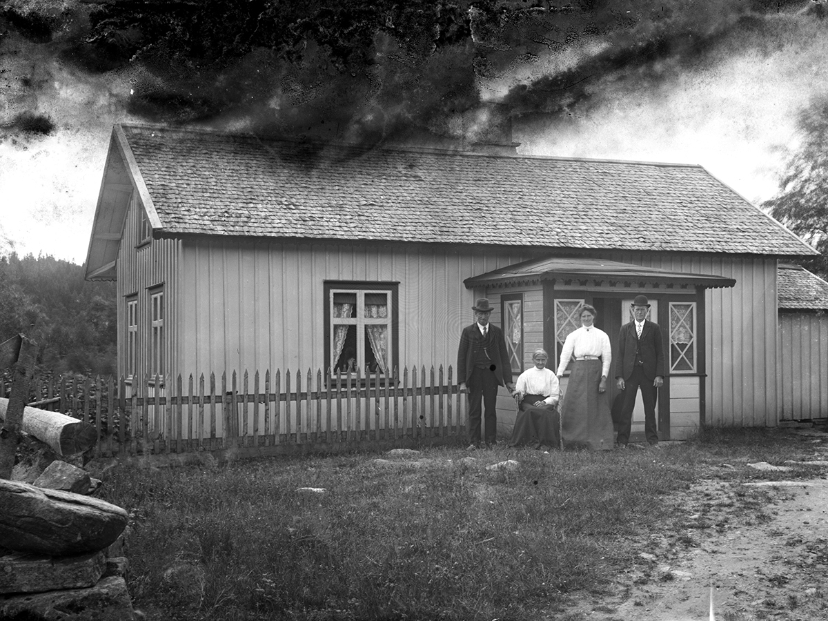 Två män och två kvinnor fotograferade utanför ett bostadshus,  torpet Hägna i Karl Gustav. Från vänster Johan August Svensson, hans hustru Karolina född Johansdotter (sittande). Kvinnan och mannen till höger i bild är parets barn Selma och Johan. Se även bild B430.