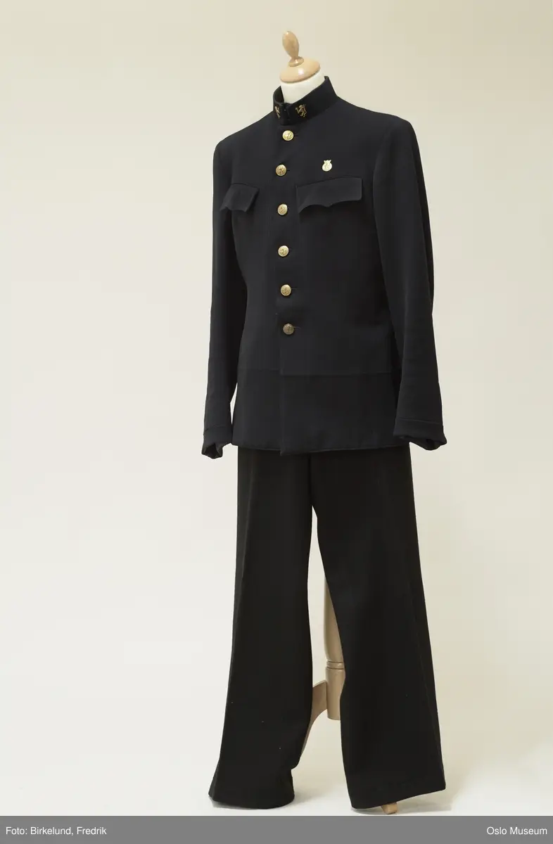 a) Jakken: Kraven oppstående, lukning med to metallhemper og kramper. Lukning foran med seks støpte, hule gultmetalls knapper med den norske løve. To brystlommer med klaffer. Lange ermer med påsydd kant. Fôr av stripet, sort silke, foran underforet med strie, ermene fôret med beige silke. På kraven foran festet to støpte gultmetalls løver.  b) Luen: Skyggelue. Pullen av mørkeblått klede med oval, flat, oppsvunget overside, sidene rette, høye, trukket med ripsbånd. Skjerm og stormrem av sort lakk. Svetterem av beige kunstlær, i pullen firkant av beige voksduk. Remmen festet med to knapper som jakkens, i fronten festet presset gultmetalls kronet skilt: Rektangel med den norske løve, på sidene fasces, bunnen med kors.