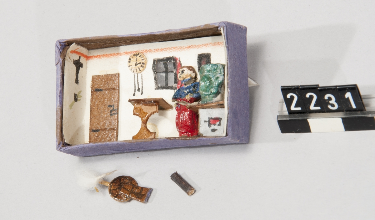 Asken märkt "Vulkan Sicherheits-Zünder", innehåller en leksaksmodell, föreställande ett rum med möbler samt en figur.