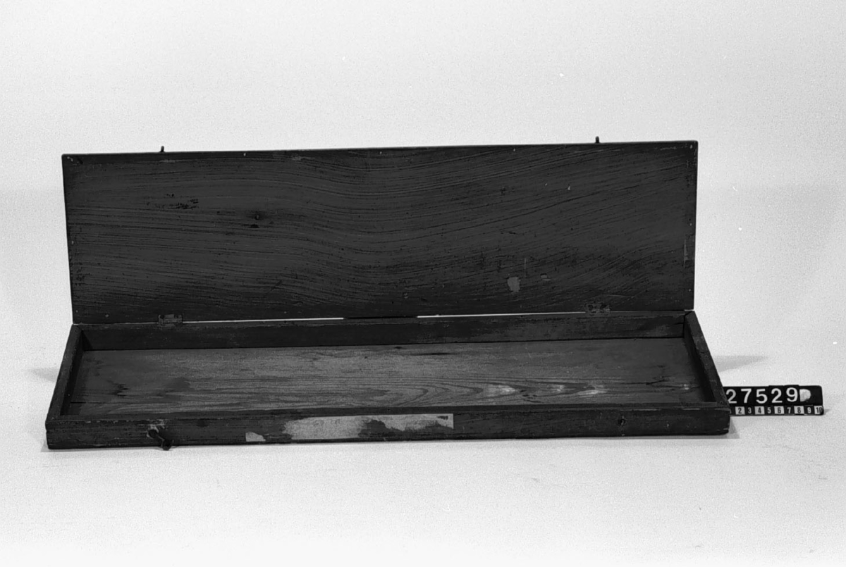 Låda av trä till förvaring av ritningsmallar, med lock på gångjärn och med kasthakar. Tidigare använd till förvaring av ritningsmallarna TM 27.524-27.527, troligen även TM 11.442-11.444. En kasthake saknas.